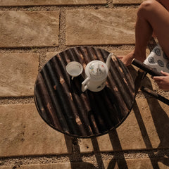 Table basse en rondins de bois brûlé Bosc Design sur une terrasse en pierre, service à café en porcelaine ancienne